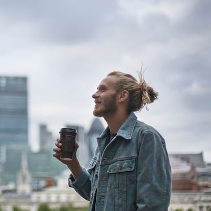 Un hombre tomando un café por la ciudad llevando su chaqueta vaquera