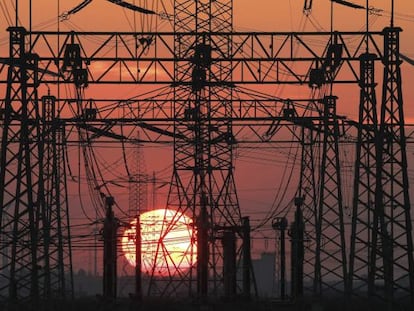 Torres de tendido eléctrico y molinos de viento durante un atardecer.