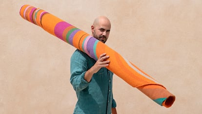 Javier Velarde, artista plástico y diseñador de alfombras, portando una de ellas frente a la fachada de mortero de cal de la casa.