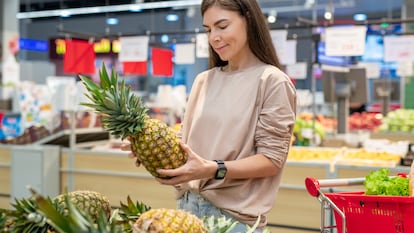 Una mujer escoge una piña en un supermercado.