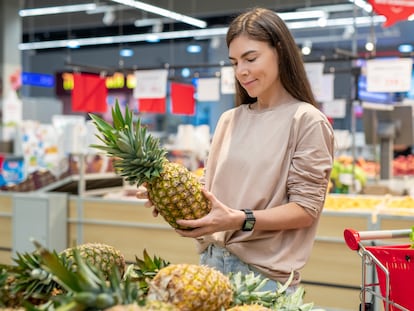 Una mujer escoge una piña en un supermercado.