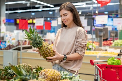 Una mujer escoge una piña en un supermercado.