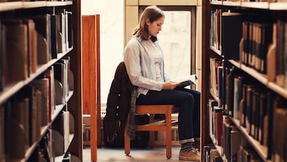 Una mujer lee un libro en una biblioteca.