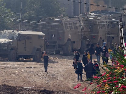 Ciudadanos palestinos, entre ellos mujeres y niños, pasan este sábado junto a tropas israelíes tras abandonar el campo de refugiados de Yenín.